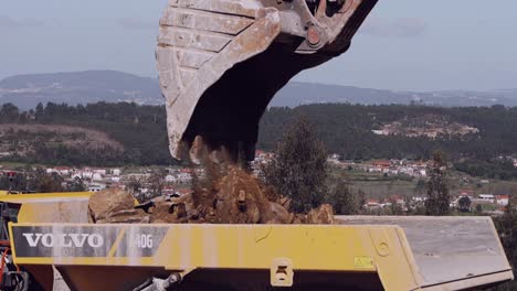 Backhoe-loader-bucket-tipping-earth-into-a-dump-truck-at-a-quarry