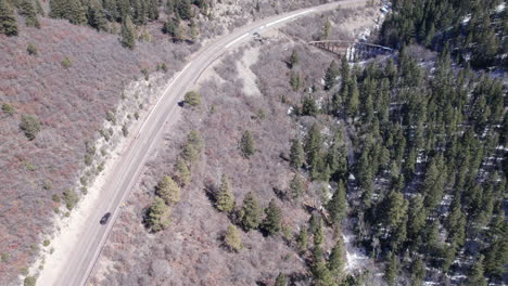 Top-down-view-of-a-rural-mountain-highway-and-historic-truss-bridge-with-narrow-gauge-railway-near-Cloudroft,-New-Mexico