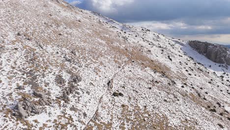 Los-Aventureros-Siguen-El-Sendero-Cubierto-De-Nieve-En-La-Región-Montañosa-Del-Peloponeso-Bajo-El-Cielo-Nublado,-Aéreo