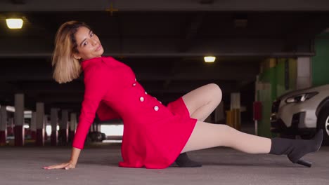 Amongst-the-cars-and-concrete-of-the-city's-parking-garage,-a-young-Hispanic-girl-stands-out-in-her-short-red-dress