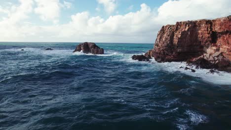 Aerial-4k-drone-establishing-shot-of-large-crashing-waves-at-Praia-da-Zimbreirinha-hidden-cliff-coastline-near-Bordeira-in-the-Algarve-region-of-Portugal