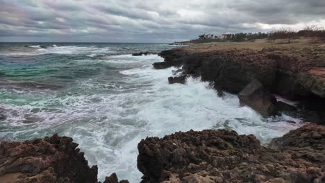 Rugged-coastline-with-waves-crashing-onto-the-rocky-shore-under-a-dramatic-cloudy-sky,-suggesting-a-powerful-and-moody-seascape