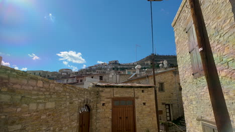 Una-Vista-Desde-Una-Calle-Del-Pueblo-De-Lefkara,-Mirando-Hacia-La-Ciudad-De-La-Ladera,-Con-Edificios-Tradicionales-De-Piedra-Y-Un-Cielo-Azul-Claro-Con-Nubes-Esponjosas.