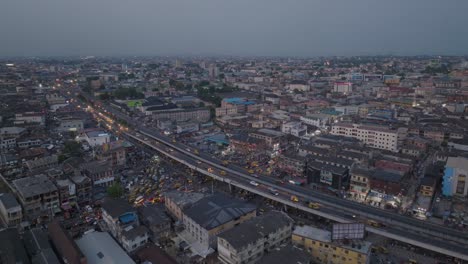 Atemberaubende-Luftaufnahme-Von-Lagos-In-Der-Abenddämmerung:-Schimmernde-Lichter-Der-Stadt,-Geschäftiger-Verkehr-Auf-Einer-Brücke,-Die-Pulsierende-Energie-Des-Städtischen-Lebens-Eingefangen