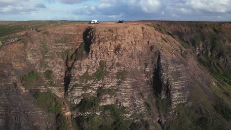 Aerial-4k-drone-view-of-camper-vans-revealing-the-sheer-drop-of-the-rugged-cliff-to-a-pristine-beach-and-gentle-ocean-waves-below-in-the-algarve-region-of-Portugal