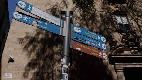 Sunlight-casting-shadows-on-a-Barcelona-street-signpost,-directing-to-landmarks