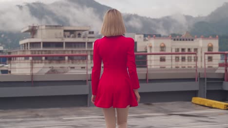 A-rooftop-in-the-bustling-city-becomes-the-stage-for-a-young-Hispanic-girl,-walking-adorned-in-a-short-red-dress