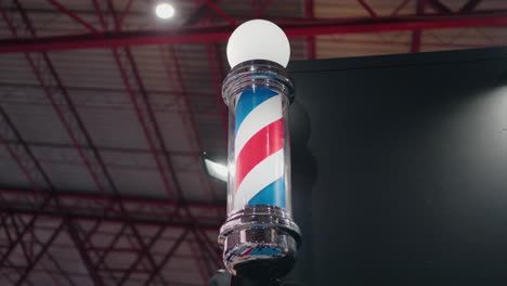 Classic-barber-pole-with-illuminated-globe-against-an-industrial-ceiling