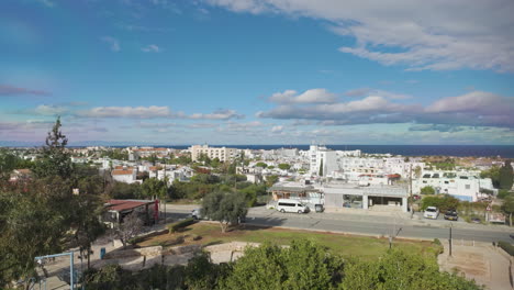 Panoramic-view-of-Protaras,-showing-a-spread-of-buildings-and-greenery-leading-to-the-blue-waters-of-the-sea,-under-a-sky-dotted-with-clouds