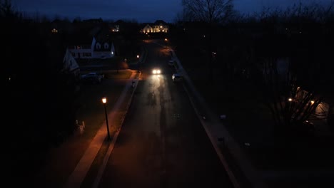 Car-with-bright-headlights-entering-neighborhood-at-night
