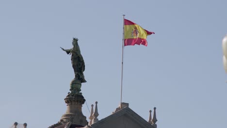 Spanish-flag-waving-next-to-a-statue-under-clear-blue-skies-in-Barcelona