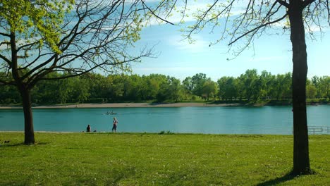 Sunny-day-at-Jarun-Lake,-Zagreb,-with-people-enjoying-a-leisurely-row-and-shoreline-stroll