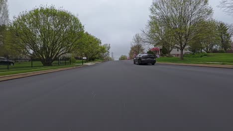 Vehículo-Negro-En-La-Carretera-En-Una-Bonita-Zona-Residencial-Americana-En-La-Temporada-De-Primavera.