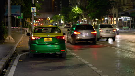 Taxi-parking-on-left-shoulder-of-road-on-an-evening-drive-with-tail-lights-and-signal-lights-on,-waiting-for-a-passenger,-while-other-cars,-motorcycles-and-motorists,-drive-by,-Bangkok,-Thailand