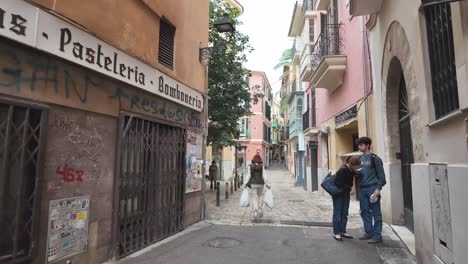 Street-in-Palma-Carrer-de-Can-Sales,-with-people-in-everyday-activities,-passing-with-groceries,-couple-with-food,-backpackers-and-tourists