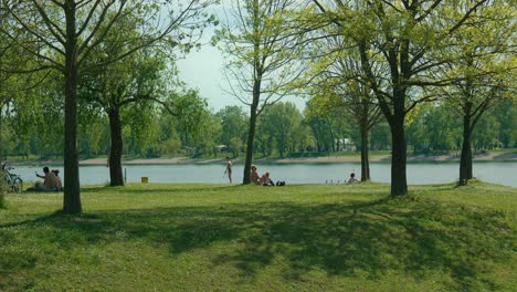 Relaxed-ambiance-at-Jarun-Lake,-Zagreb,-with-people-lounging-under-spring-foliage