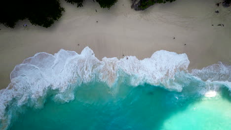 Kleine-Leute-Entspannen-Sich-Am-Sandstrand,-Während-Starke-Meereswellen-Am-Kelingking-Strand-Brechen