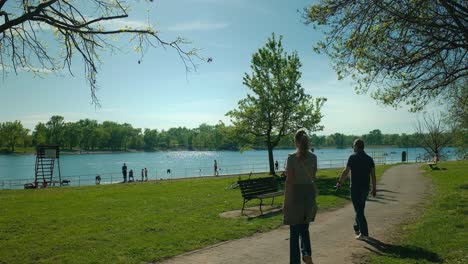 Día-Sereno-En-El-Lago-Jarun,-Con-Gente-Paseando-Y-Disfrutando-Del-Paseo-Marítimo,-Frente-A-Un-Cielo-Azul-Claro-En-Zagreb,-Croacia.