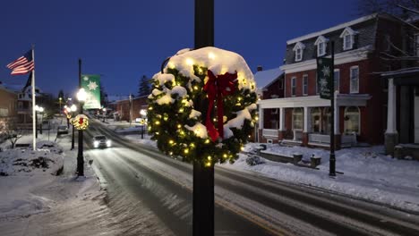 Corona-De-Navidad-Cubierta-De-Nieve-En-La-Ciudad-Americana-Con-Bandera-Ondeando-En-Segundo-Plano.