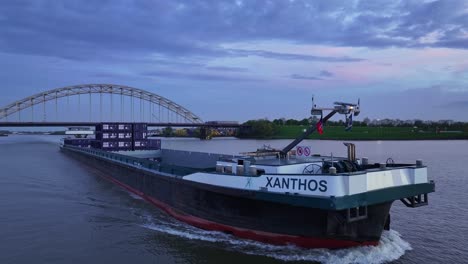 Cargo-Ship-Xanthos-Cruising-River-In-Alblasserdam,-Netherlands-At-Sunset---Drone-Shot