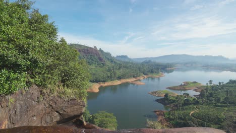 Atemberaubende-Drohnenaufnahme-Der-Gartmore-Falls-In-Sri-Lanka,-Mit-üppigem-Grün,-Orangefarbenem-Sand-Und-Felsen-Vor-Einem-Strahlend-Blauen-Himmel