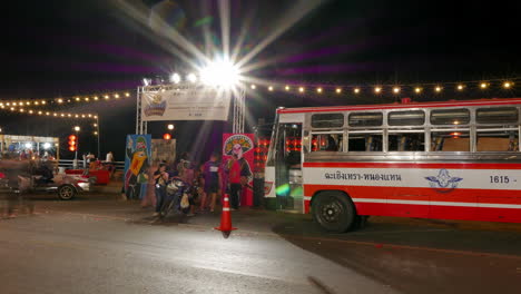 Hyperlapse-of-a-riverside-night-market-where-shoppers-and-commuters-are-standing-in-front-of-a-bus,-a-local-transportation-in-Chachoengsao-province-in-Thailand