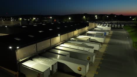 Drone-flight-over-United-Parcel-Service-logistics-location-with-parking-trucks-after-sunset-in-USA
