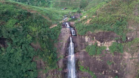 Atemberaubende-Drohnenaufnahme-Der-Gartmore-Falls-In-Sri-Lanka,-Mit-üppigem-Grün,-Orangefarbenem-Sand-Und-Felsen-Vor-Einem-Strahlend-Blauen-Himmel