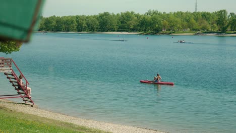 lone-paddler-on-a-red-kayak-enjoys-the-tranquility-of-Jarun-Lake-with-distant-rowers-and-green-shores