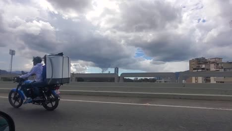 Dos-Hombres-En-Una-Motocicleta-Que-Llevaban-Una-Lavadora-Mientras-Corrían-Por-La-Carretera,-Caracas,-Venezuela.