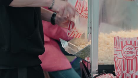 Person-scooping-fresh-popcorn-from-a-machine-into-a-striped-bag