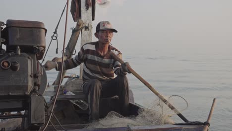 Un-Viejo-Pescador-Tradicional-Disfruta-De-Un-Cigarrillo-Mientras-Vierte-Hábilmente-Redes-De-Pesca-Y-Dirige-El-Barco-Simultáneamente,-Yo