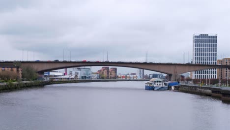 Busy-traffic-driving-over-bridge-and-the-River-Clyde-lined-by-buildings,-businesses-and-high-rise-offices-in-Glasgow-city,-Scotland-UK