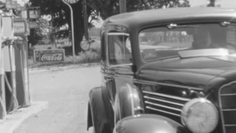 Una-Mujer-Conduce-Un-Automóvil-Clásico-Después-De-Cargar-Gasolina-En-La-Estación-Durante-El-Día-En-Los-Años-1930.