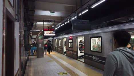 People-walk-outside-Buenos-Aires-City-underground,-train-waits-passengers-seated-Station-with-European-heritage-architectural-style