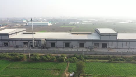 aerial-drone-view-The-drone-camera-is-moving-backwards-and-there-are-green-fields-on-the-right-side-of-the-factory-and-a-small-river