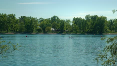 Rowers-glide-on-the-calm-waters-of-Jarun-Lake-in-Zagreb,-framed-by-lush-trees-and-clear-skies