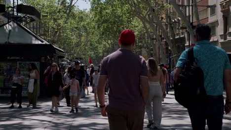 Bustling-street-scene-on-La-Rambla,-Barcelona-with-pedestrians-and-shaded-trees,-sunny-day