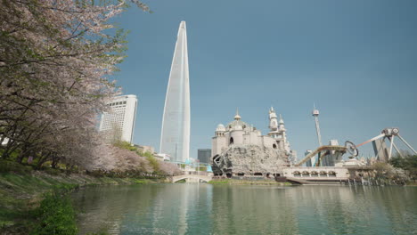 Seokchon-Lake,-Lotte-World-Amusement-Park,-and-Lotte-Tower-During-Sakura-Blooming-Spring-Day-in-Seoul,-South-Korea