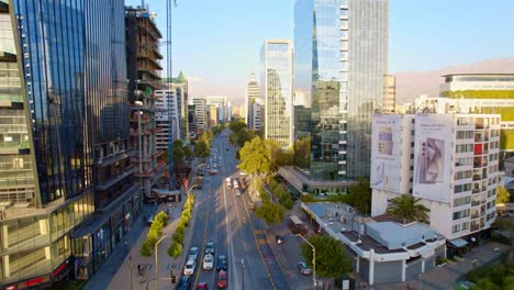 Apoquindo-avenue-in-las-condes,-bustling-with-traffic-and-surrounded-by-modern-skyscrapers-at-sunset,-aerial-view