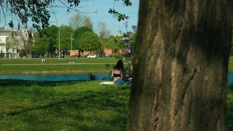 Couple-relaxing-on-a-sunny-day-by-Jarun-Lake-in-Zagreb,-with-vibrant-park-life