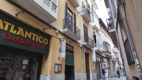 Traditional-architecture-in-Palma-De-Mallorca,-narrow-street-with-a-cocktail-bar,-pedestrian,-and-balconies