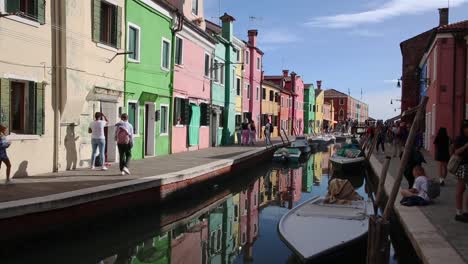Tourist-walk-by-colorful-vibrant-houses-along-canal-on-Burano-island-Venice,-Italy