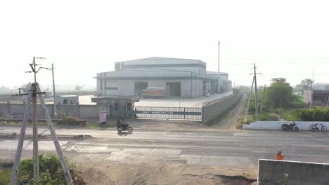 aerial-drone-view-Drone-camera-moving-upwards-from-the-front-showing-a-large-factory-A-truck-loaded-with-food-is-visible-in-the-factory-and-large-fields-are-visible-behind-the-factory