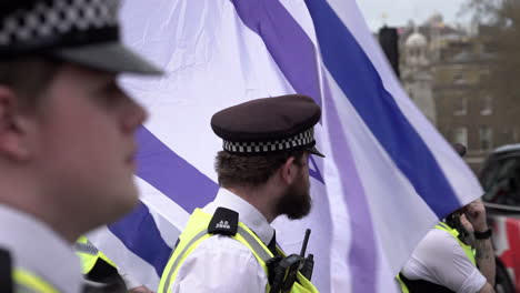 Metropolitan-police-officers-stand-in-line-on-a-cordon-next-to-blue-and-white-Star-of-David-Israeli-flags-fluttering-in-the-wind-during-a-counter-protest-to-the-annual-Al-Quds-day-demonstration