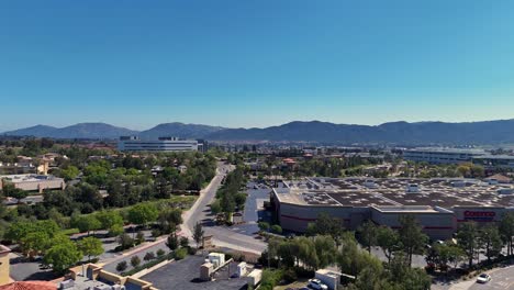 Drohnenflug-Entlang-Der-Promenadenstraße-Hinter-Dem-Costco-In-Temecula,-Kalifornien,-Von-Hinter-Dem-Lagerhaus-Zum-Seitlichen-Parkplatz-Mit-Bäumen-Und-Benachbarten-Bürogebäuden-Und-Hügeln-Im-Hintergrund