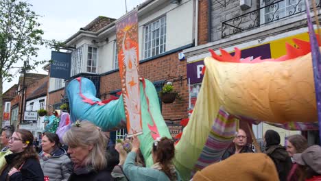 Colorful-dragon-moving-through-busy-streets-of-Glastonbury-town-during-Beltane-May-Day,-beginning-of-summer,-celebrations-and-festival-in-Somerset-UK