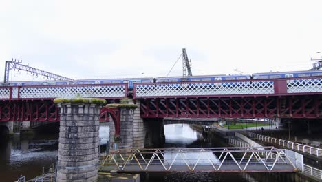 Scottish-passenger-train,-public-transport,-slowly-traveling-over-River-Clyde-and-intricate-bridge-in-Glasgow-city,-Scotland