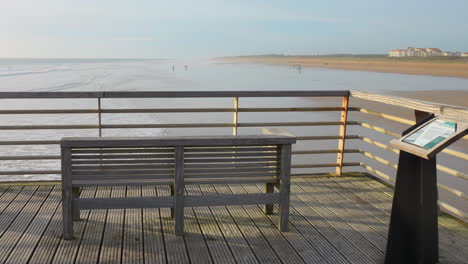 Empty-wooden-bench-overlooking-a-serene-beach-in-Saint-Jean-de-Monts-during-daylight,-clear-sky