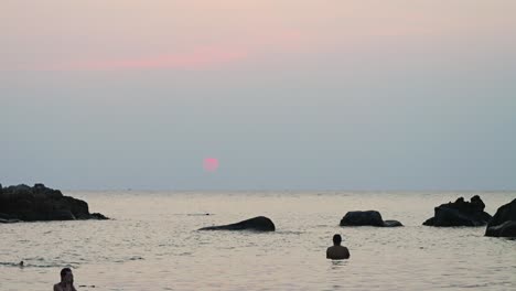 Ruhige-Landschaft-Am-Strand-Bei-Sonnenuntergang-Mit-Menschen-Und-Springenden-Fischen